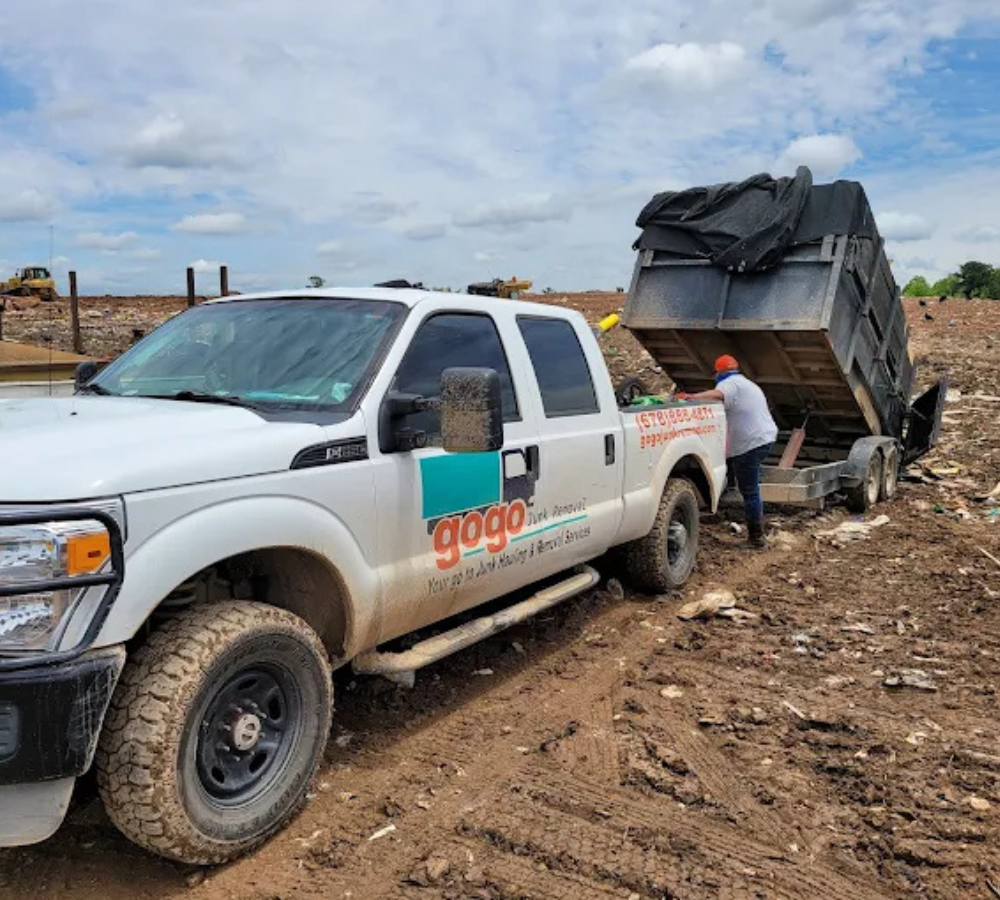 GoGo Junk Removal technician operating a remote-controlled dump trailer to unload debris at the landfill, with truck and trailer visible.