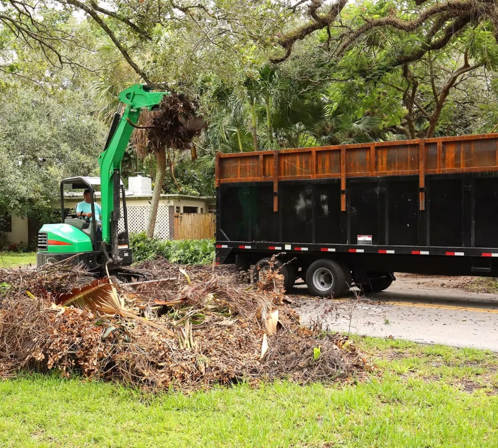 Bulk yard debris being loaded onto a GoGo Junk Removal trailer using an excavator.